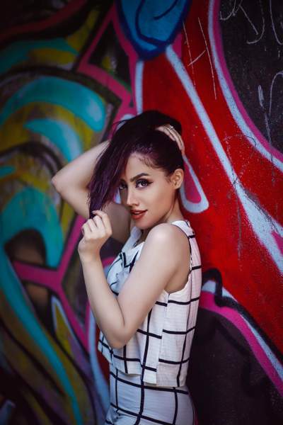 Woman wearing white and black outfit posing in front of colourful graffiti covered wall
