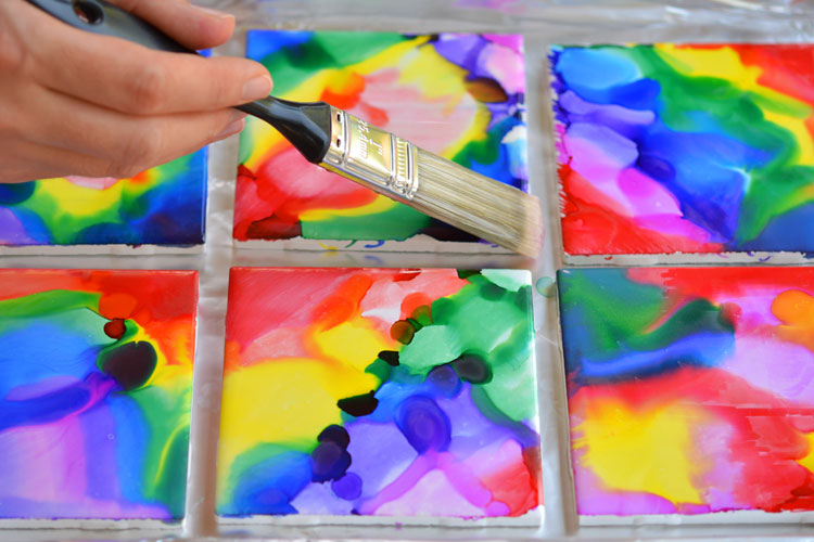 Hand holding paint brush painting squares in rainbow colors.
