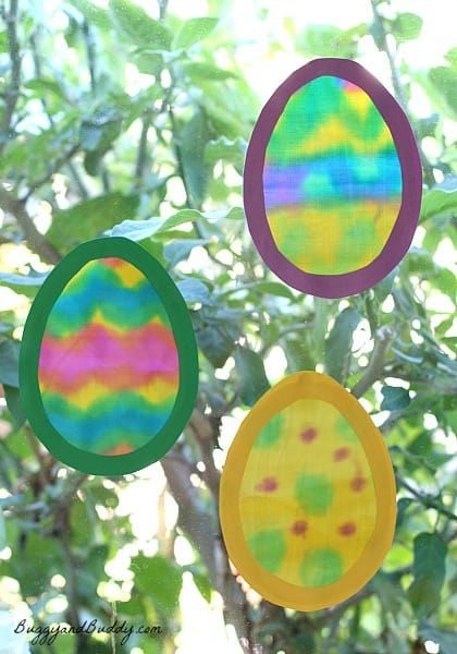 Three colorful translucent eggs hanging in front of a window.