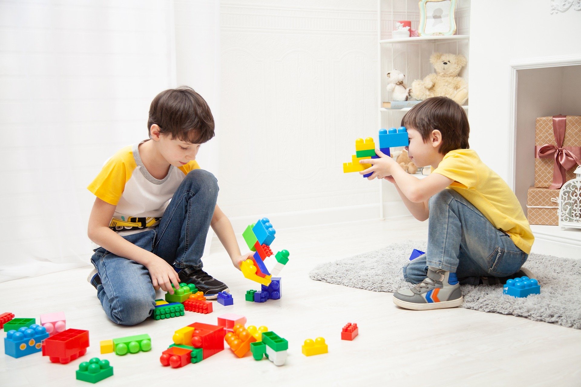 Two boys playing with plastic bricks in a white room.