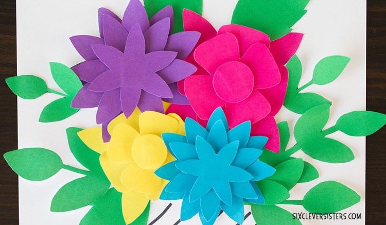 Four brightly-colored paper flowers on green foliage.