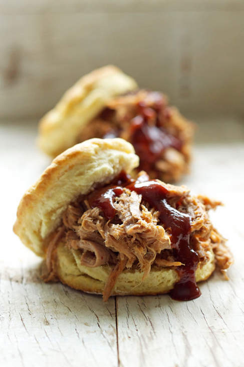Two biscuit sandwiches filled with pulled pork garnished with brown sauce.